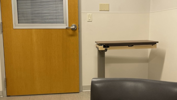 Interior common area with multiple upholstered chairs with wood frames, small tables, mission statement wall display, and patient safety signage