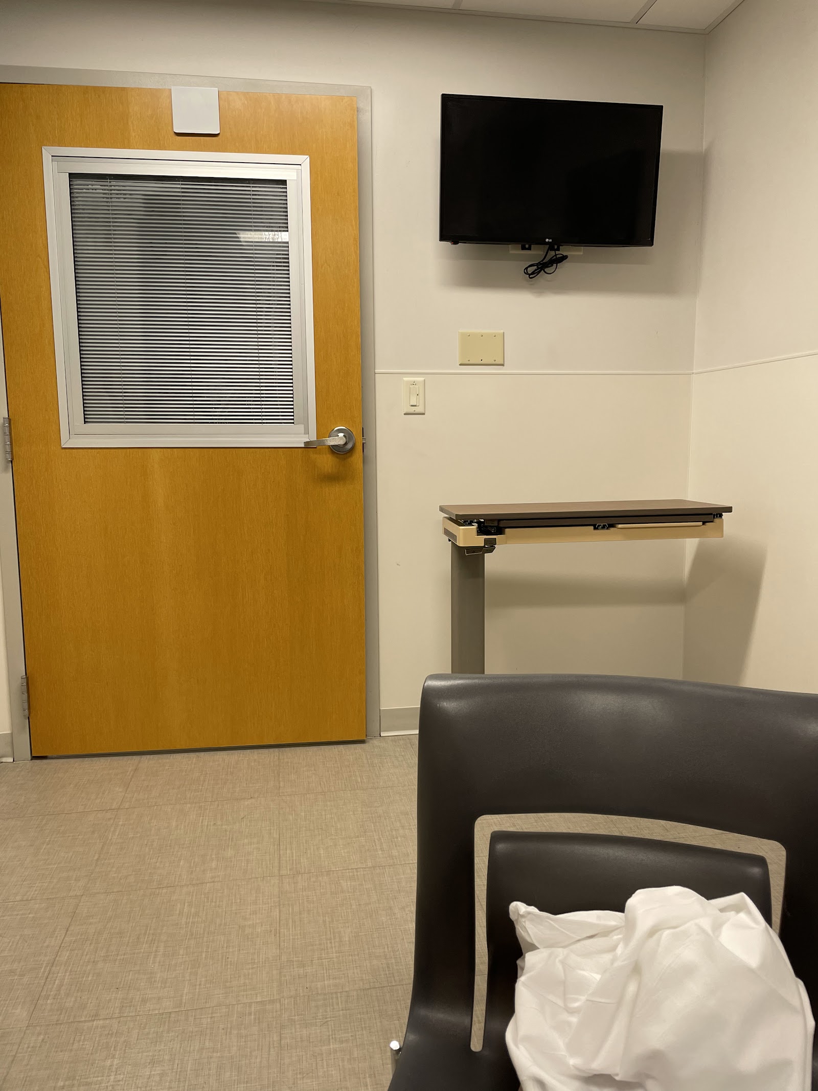 Interior common area with multiple upholstered chairs with wood frames, small tables, mission statement wall display, and patient safety signage