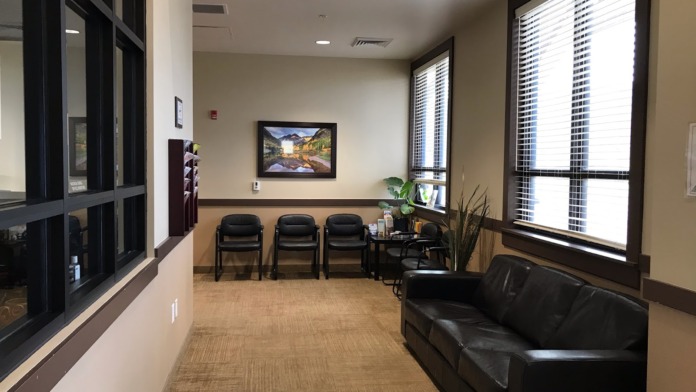 Interior waiting area with comfortable seating, landscape artwork, windows with blinds, and professional furnishings