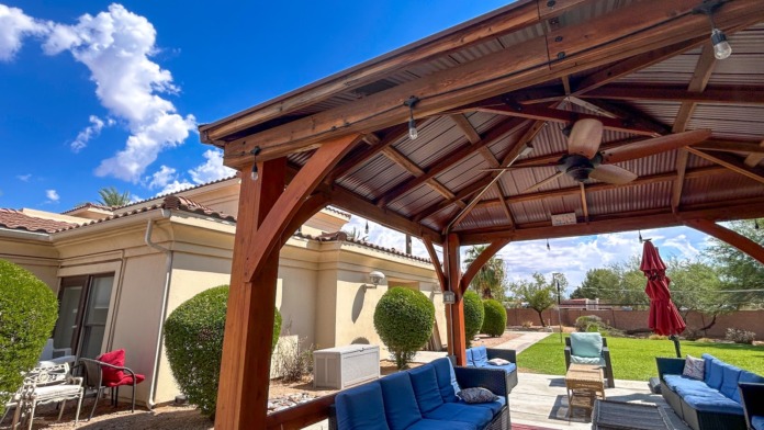 Outdoor covered patio area with wooden pergola, cushioned lounge seating, and manicured landscaping