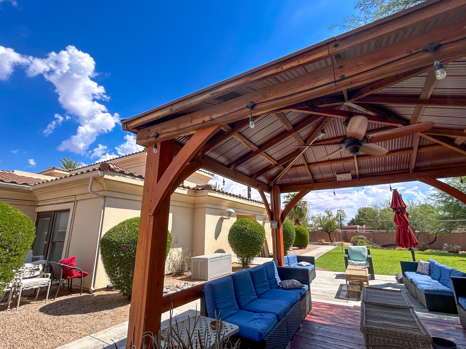 Outdoor covered patio area with wooden pergola, cushioned lounge seating, and manicured landscaping