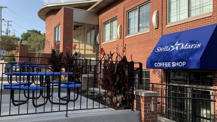 Exterior patio area with blue picnic tables, landscaping, and brick building facade with entrance
