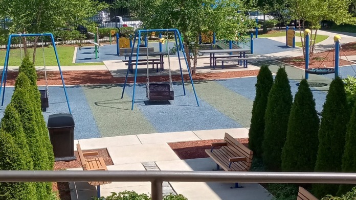 Outdoor recreation area with multiple swings, play equipment, shade structures, and landscaping