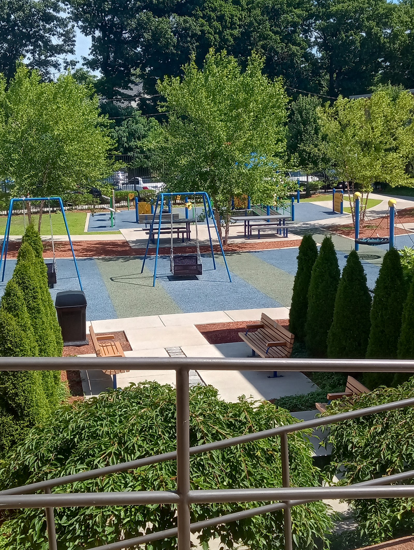 Outdoor recreation area with multiple swings, play equipment, shade structures, and landscaping