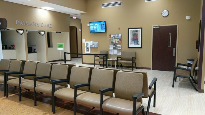 Interior waiting room with beige upholstered chairs, reception desk, and Primary Care signage on wall