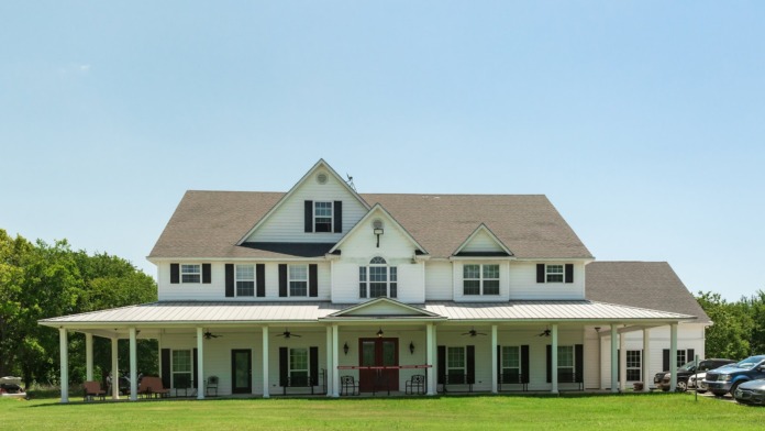 Exterior of large white farmhouse-style residence with covered porch and multiple windows