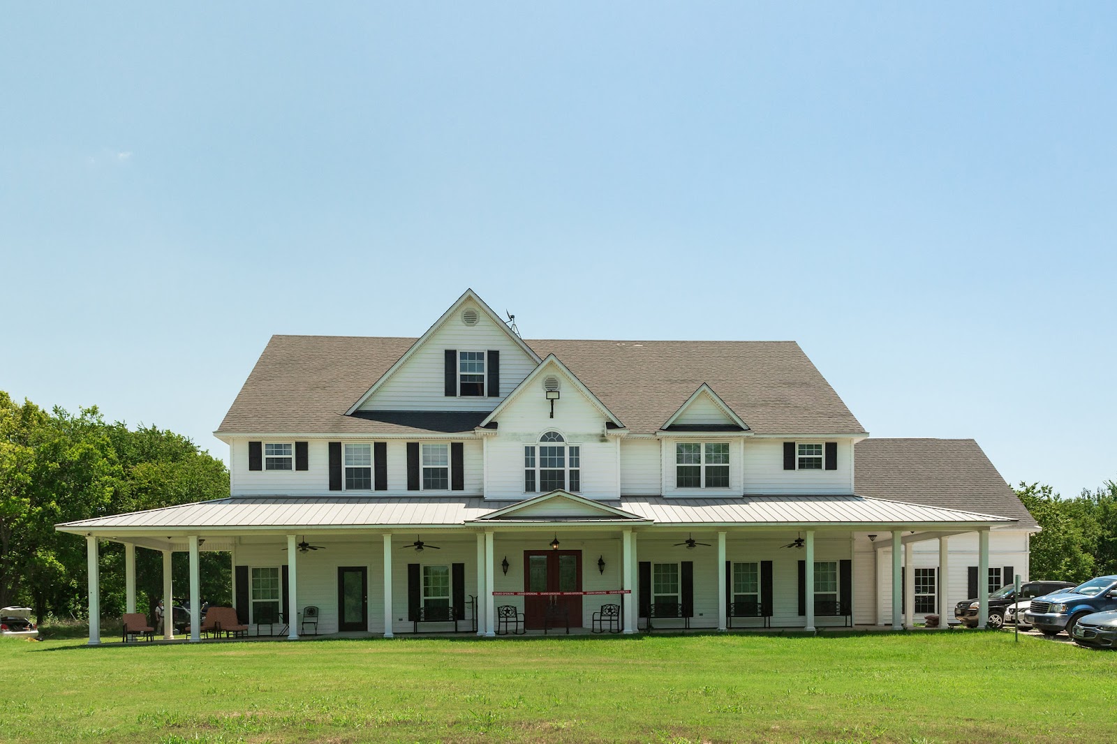 Exterior of large white farmhouse-style residence with covered porch and multiple windows