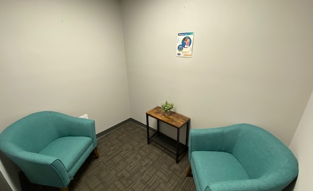 Interior private room with two turquoise armchairs, small wooden table with plant, and decorative wall art