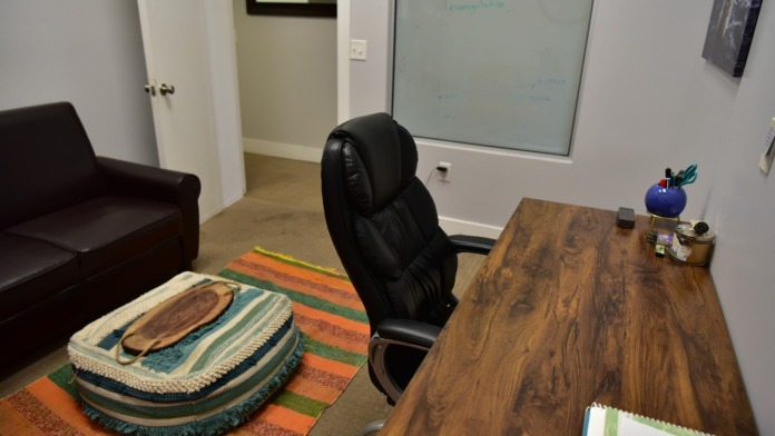 Interior office space with wooden desk, black chair, dark sofa, whiteboard, and patterned area rug.