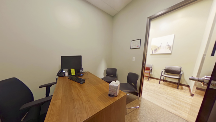 Interior counseling office with desk, computer, wooden furniture, picture frame, and brown door