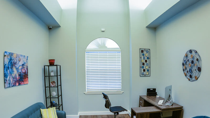 Interior professional office space with natural lighting, desk setup, comfortable seating, and therapeutic artwork on walls