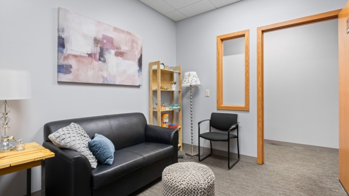 Interior counseling space with black sofa, wooden shelving, abstract artwork, and wooden-framed doorways