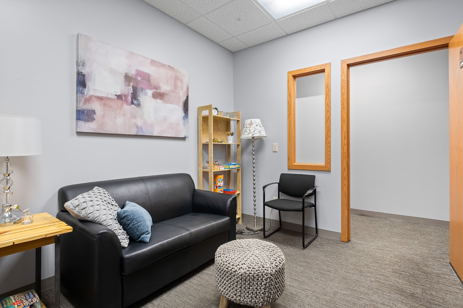Interior counseling space with black sofa, wooden shelving, abstract artwork, and wooden-framed doorways
