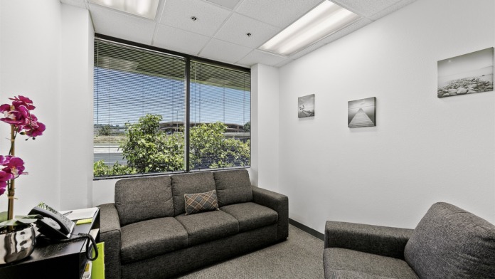 Interior private office with desk phone, flower arrangement, couch, window view, and nature photography