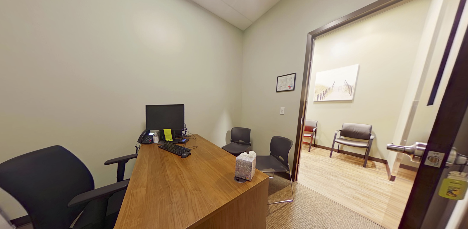 Interior office with wooden desk, chair, and doorway opening to adjacent reception or waiting space