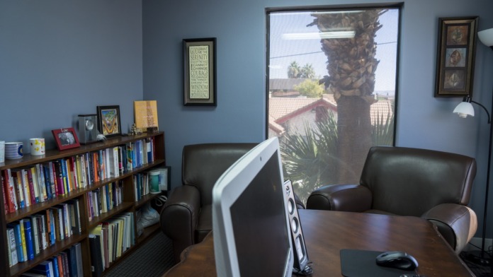 Interior office with bookshelf, leather armchairs, desk with computer, and window view to exterior landscape