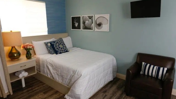Interior patient bedroom with bed, nightstand, window seating area, and calming blue and white color scheme