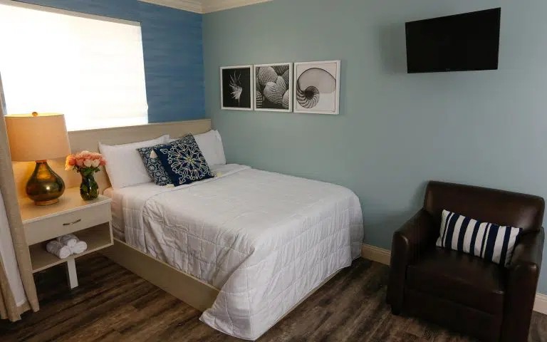 Interior patient bedroom with bed, nightstand, window seating area, and calming blue and white color scheme
