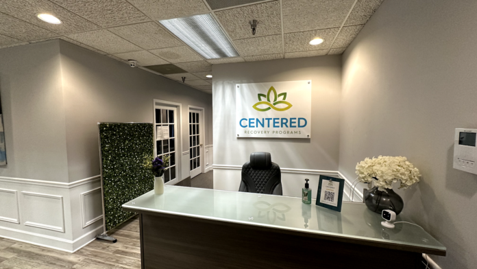 Interior reception area with white desk, branded signage, green plant wall feature, and professional seating