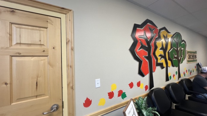 Interior room with wooden door, program signage, colorful leaf artwork on wall, and seating for activities or groups