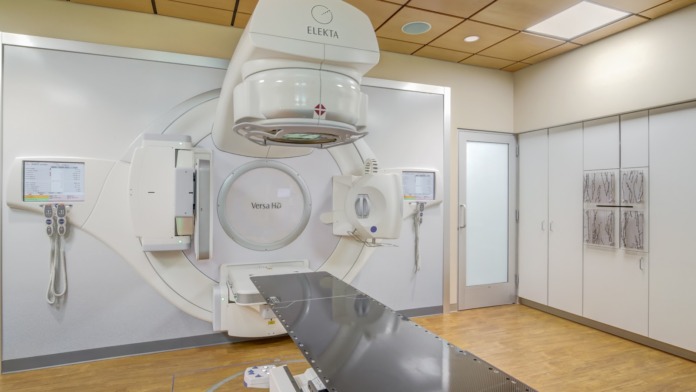 Interior medical suite with Elekta Versa HD linear accelerator machine, treatment table and clinical monitoring equipment