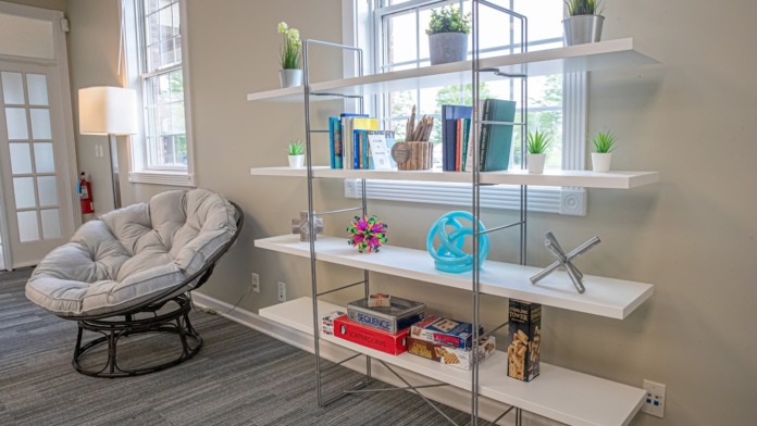 Interior reading space with comfortable round chairs, shelving with books and plants, multiple windows with natural light