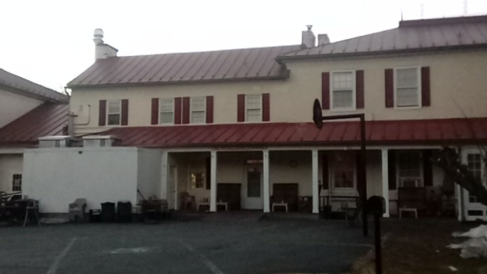 Exterior rear view showing covered patio structure with white columns, red metal roof, stone facade, and parking area