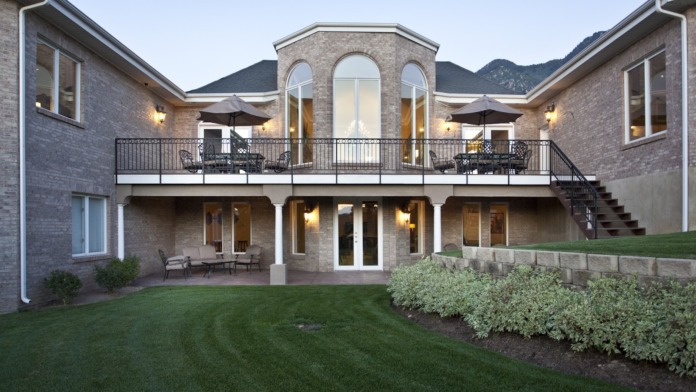 Exterior rear view showing multi-level brick building with upper and lower patios, umbrellas, seating areas, and manicured grounds