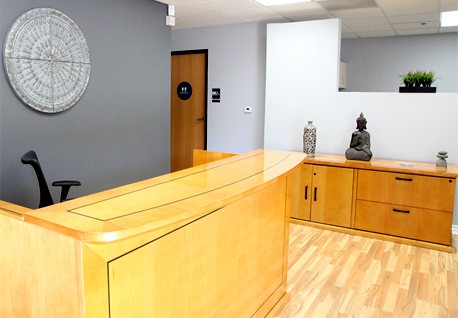 Interior reception desk with honey wood finish, decorative clock on wall, and minimal furnishings in professional office setting