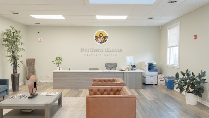 Interior reception desk with Northern Illinois Recovery Center logo and signage, comfortable seating area, and plants