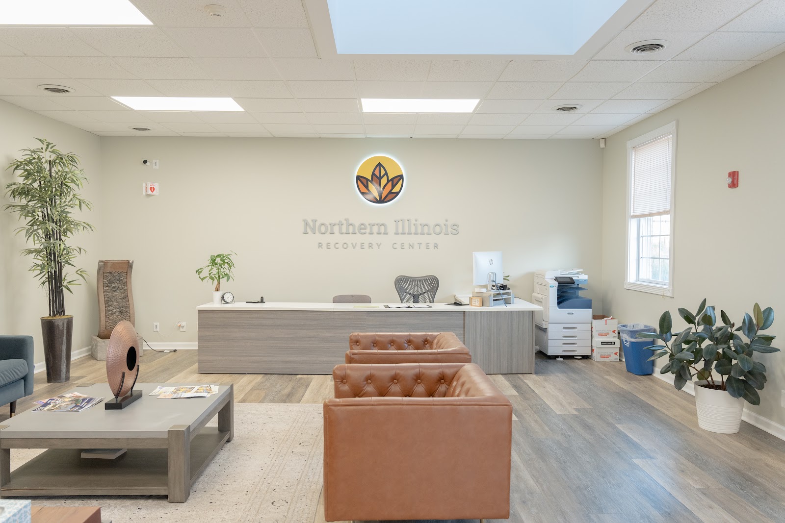 Interior reception desk with Northern Illinois Recovery Center logo and signage, comfortable seating area, and plants
