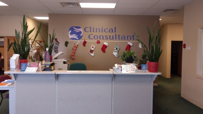 Interior reception desk with Clinical Consultants logo on wall, decorative plants, holiday decorations, and seating area