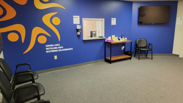 Interior reception waiting area with blue accent walls, Spero Health logo and mission statement, intake desk, and seating chairs