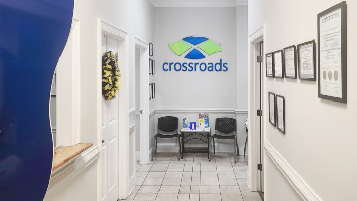 Interior reception hallway with Crossroads Treatment Centers logo on wall, tiled flooring, white doors, and seating area