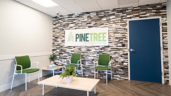 Interior reception space featuring Pine Tree Recovery Center logo on accent wall with modern seating and natural lighting