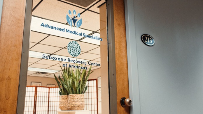 Interior reception space showing wooden door frame, decorative plant, and Suboxone Recovery Center of Arkansas logo on glass