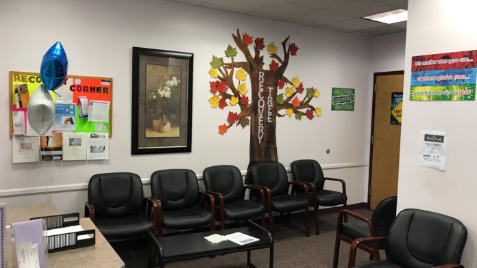 Interior waiting room with black leather chairs arranged in rows, white walls, and motivational tree decoration.