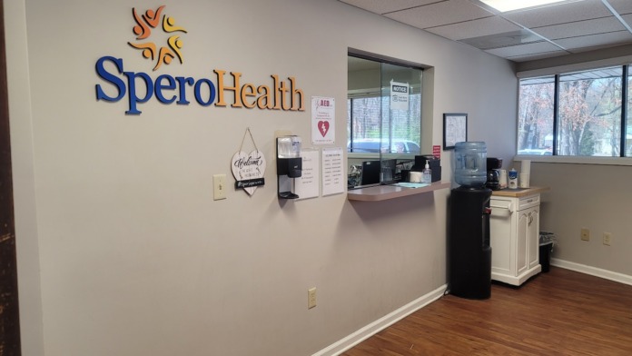 Interior reception area with SperoHealth signage, desk, coffee station, and windows overlooking parking area