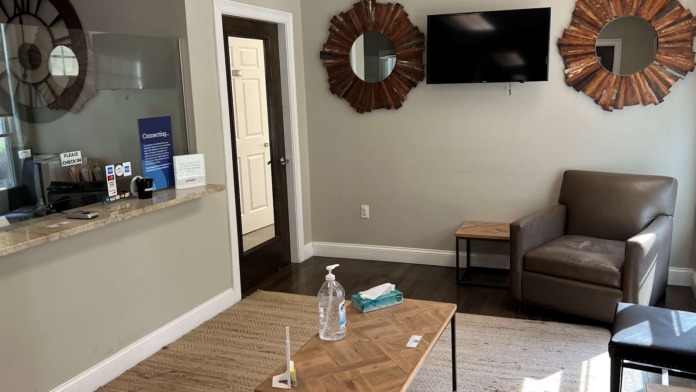 Interior reception space with check-in counter, seating, wall decor, and television for patient information
