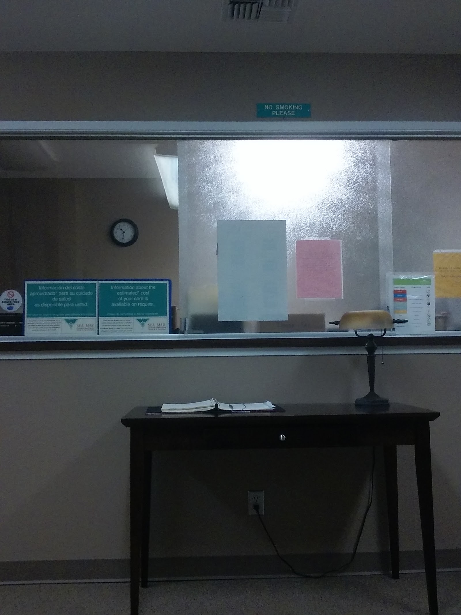 Interior office area showing reception window, clock on wall, and desk with materials and informational signage