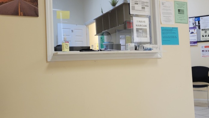 Interior reception service window showing office equipment, plants, and patient check-in area with motivational wall signage