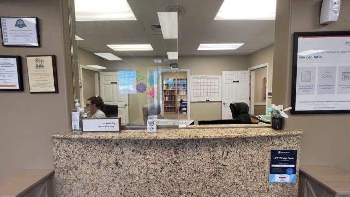 Interior front desk with granite countertop, staff workspace, wall-mounted displays, and library with books visible in background