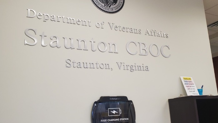 Interior office space with department signage, VA seal, charging station, and work desk with materials