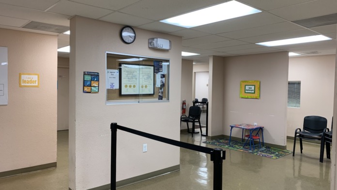 Interior reception area with check-in window, seating area with chairs, and informational bulletin board displaying treatment center announcements