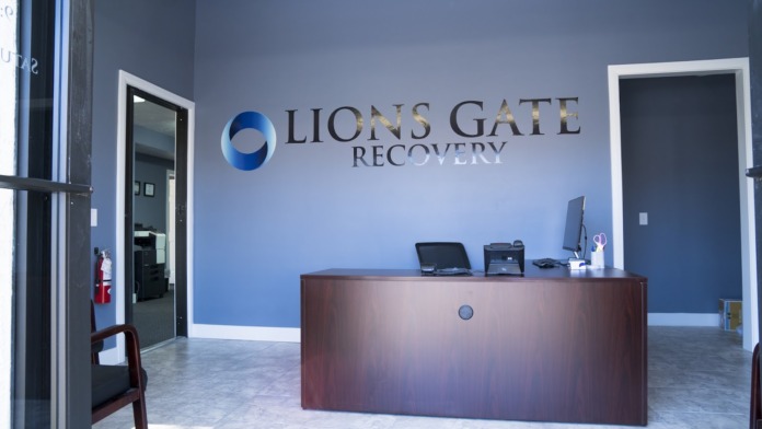 Interior reception desk with Lions Gate Recovery signage on blue wall, featuring desk with computer and office materials