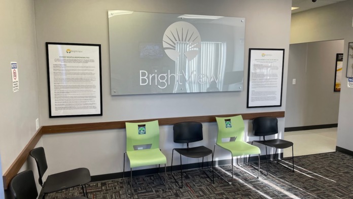 Interior reception area with framed informational posters, wall signage, green and black seating, and professional healthcare setting