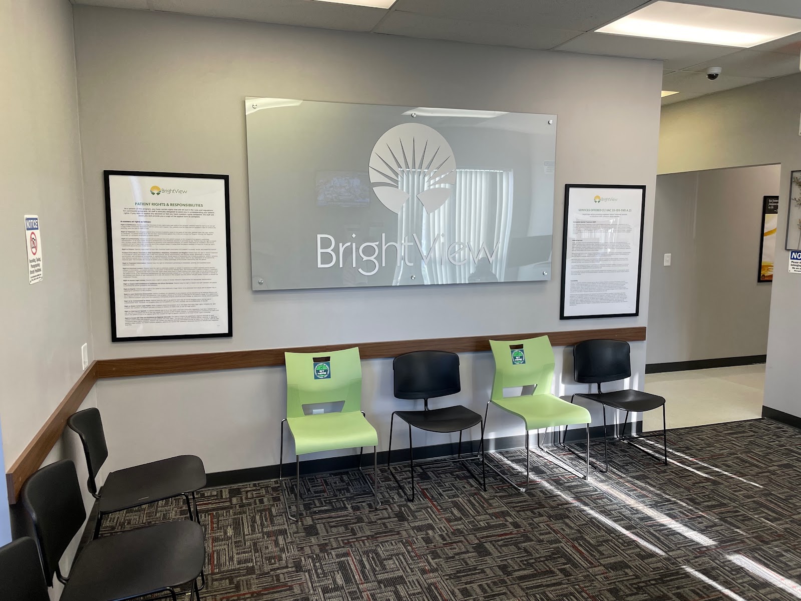 Interior reception area with framed informational posters, wall signage, green and black seating, and professional healthcare setting