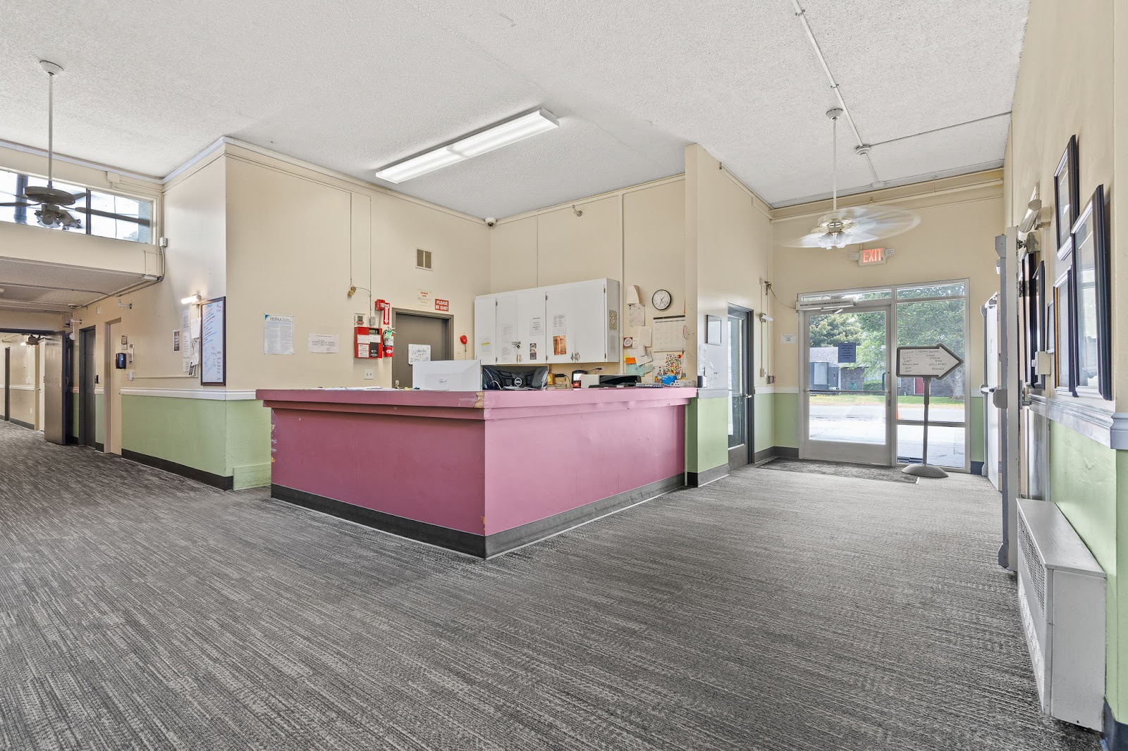 Interior reception area with pink desk, cream walls with green wainscoting, exit signage, and glass entry doors