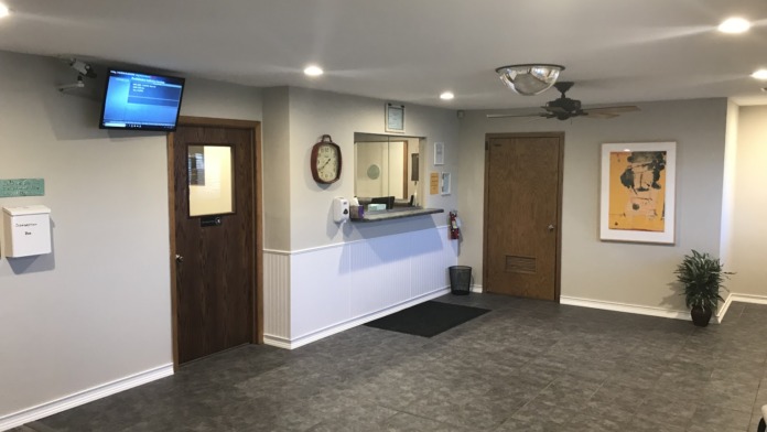 Interior reception area with front desk, wall-mounted television, clock, framed artwork, and potted plant decoration