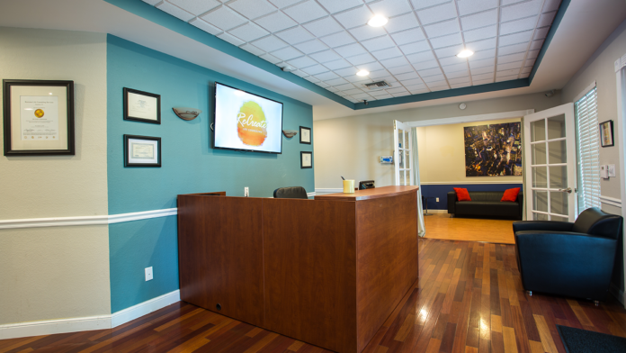 Interior reception area with turquoise accent wall, wooden reception desk, framed certifications and diplomas, and seating areas visible.
